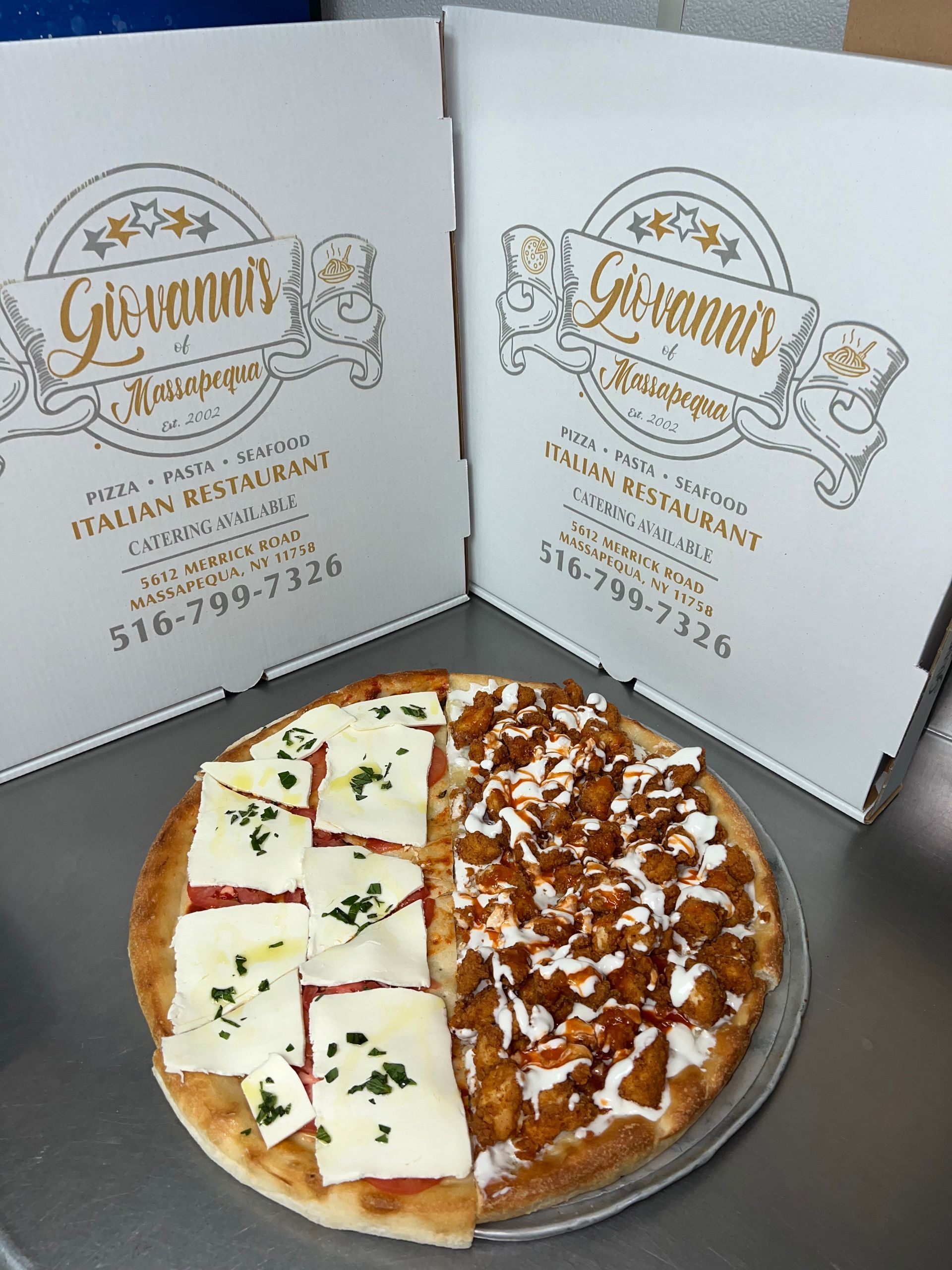 Two pizza boxes behind a half-and-half pizza with white cheese and meat toppings