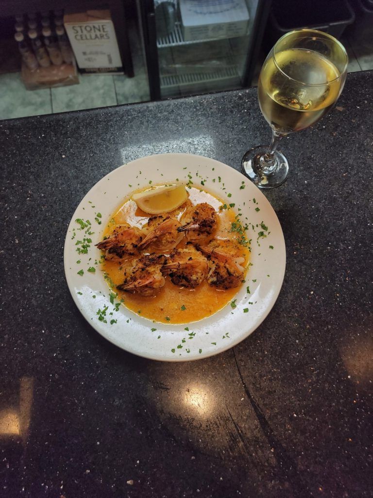 Plate of fried seafood with lemon on a dark table beside a glass of white wine