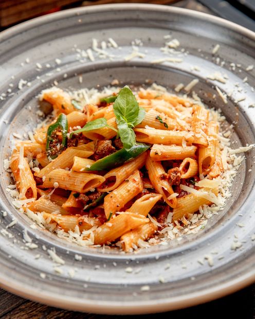 Pasta penne with tomato sauce, basil, and grated cheese in a gray bowl