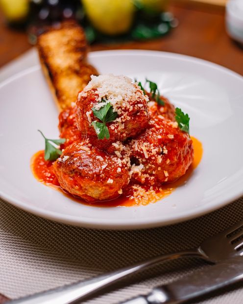 Plated pasta with red sauce, grated cheese, and basil, served beside toasted bread on a dining table.
