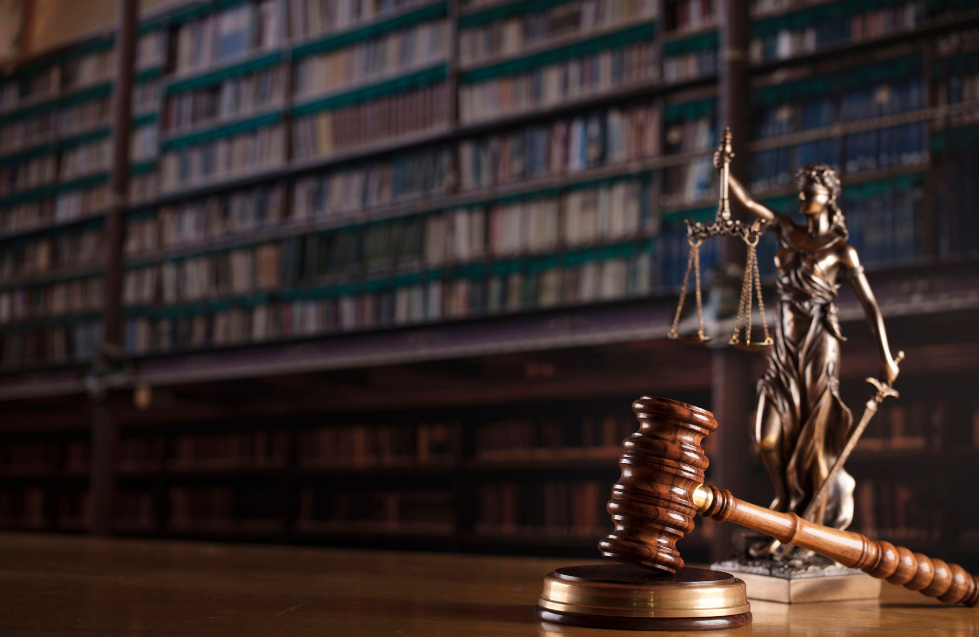 Lady Justice statue beside a gavel and stacked coins in a law library