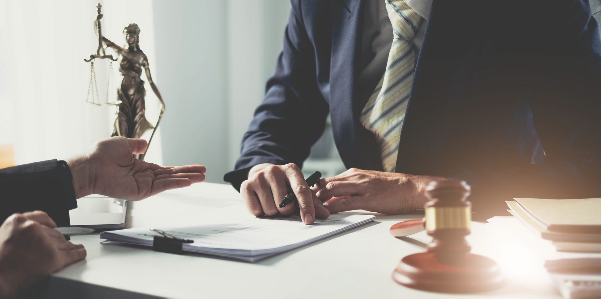 Lawyer’s desk with handshakes, gavel, and justice statue in a bright office