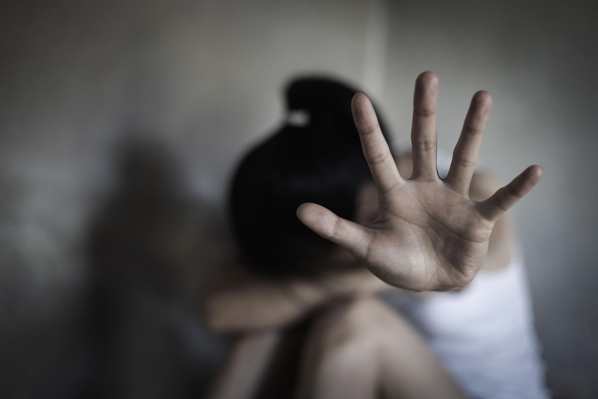 Person with raised hand in foreground, seated and blurred in the background, suggesting distress or a plea for help