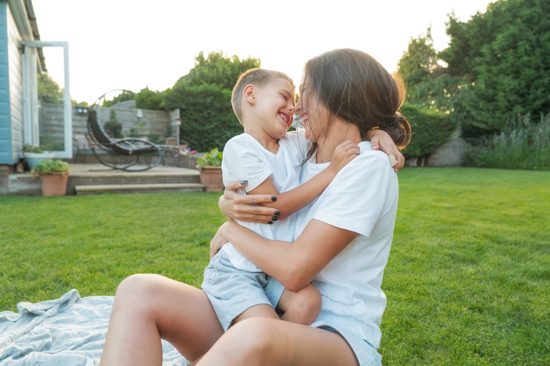 Adult holding a smiling child on a grassy lawn in a sunny backyard