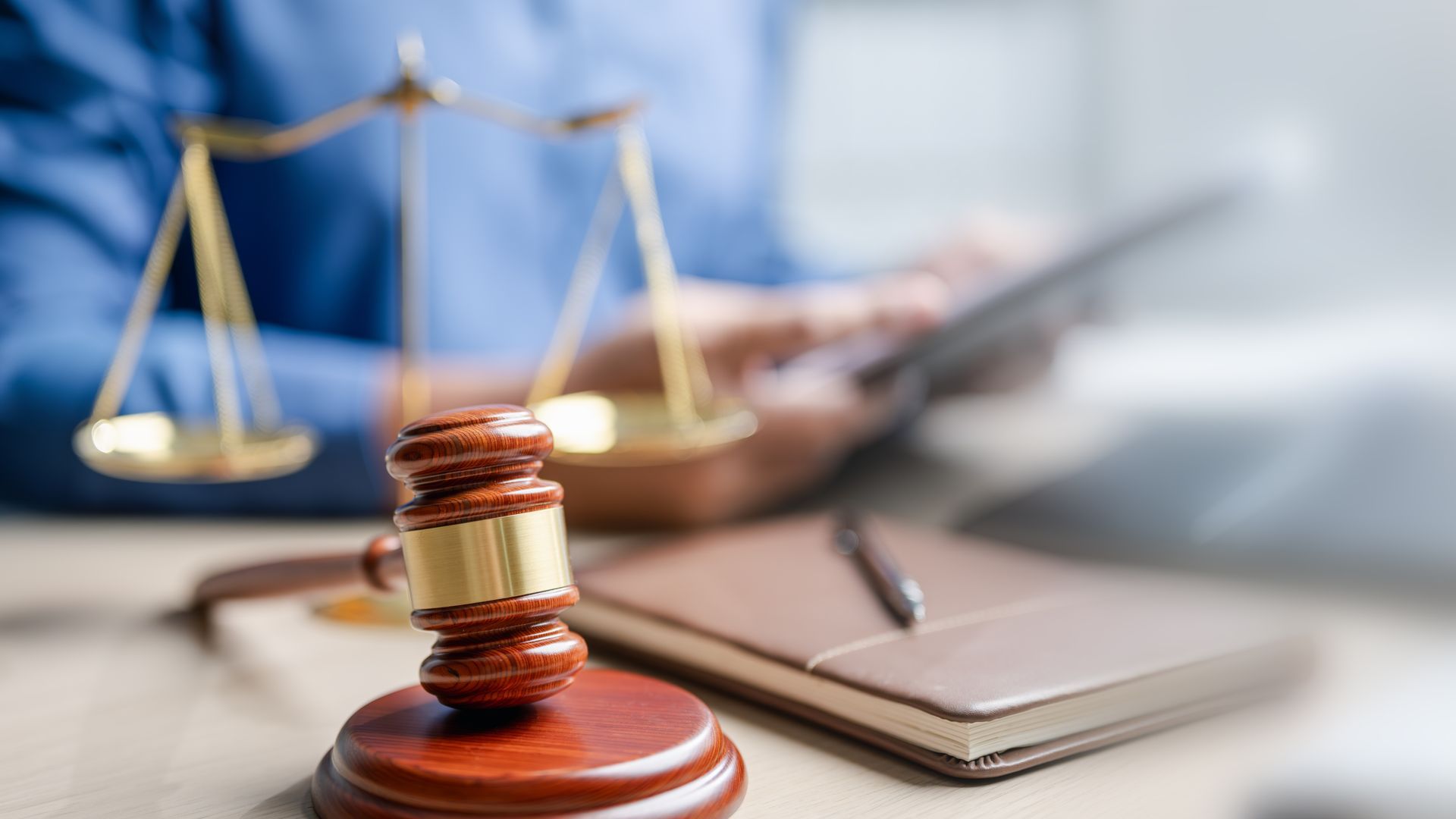 Gavel and scales of justice beside a law book on a desk in a courtroom-style setting