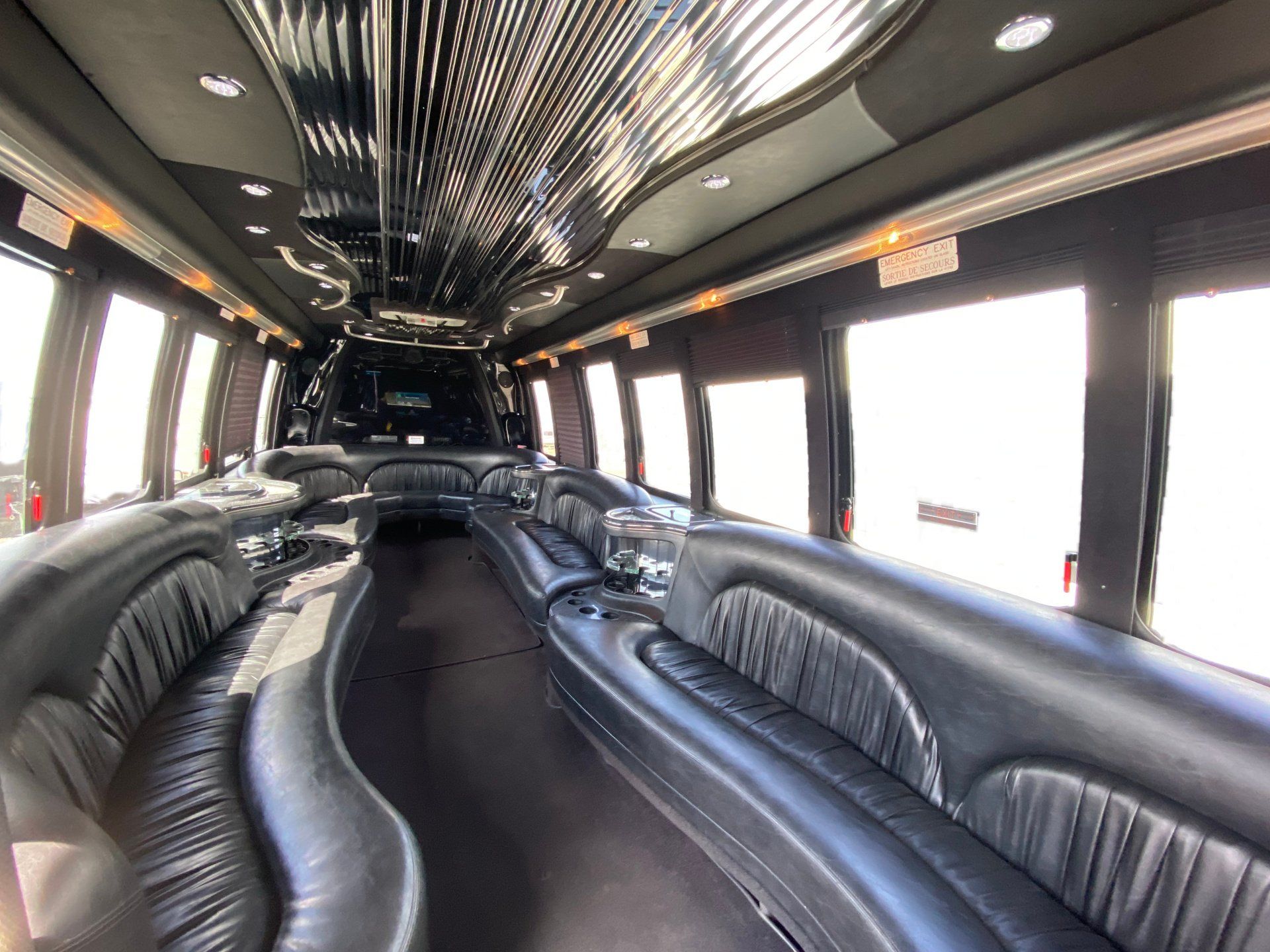 The inside of a limousine with black leather seats and a long couch.
