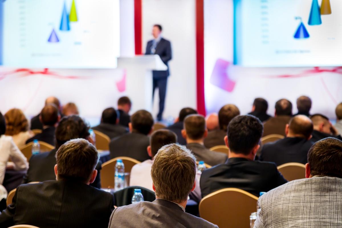 man at podium on stage speaking to audience