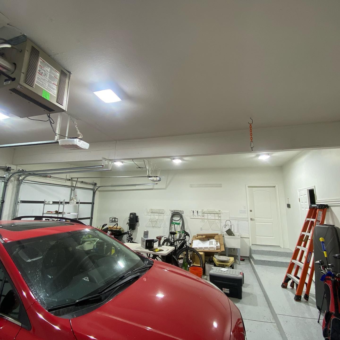 A red car is parked in a garage next to a ladder.