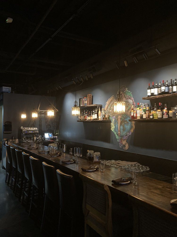 A long wooden bar in a restaurant with a lot of bottles on shelves.