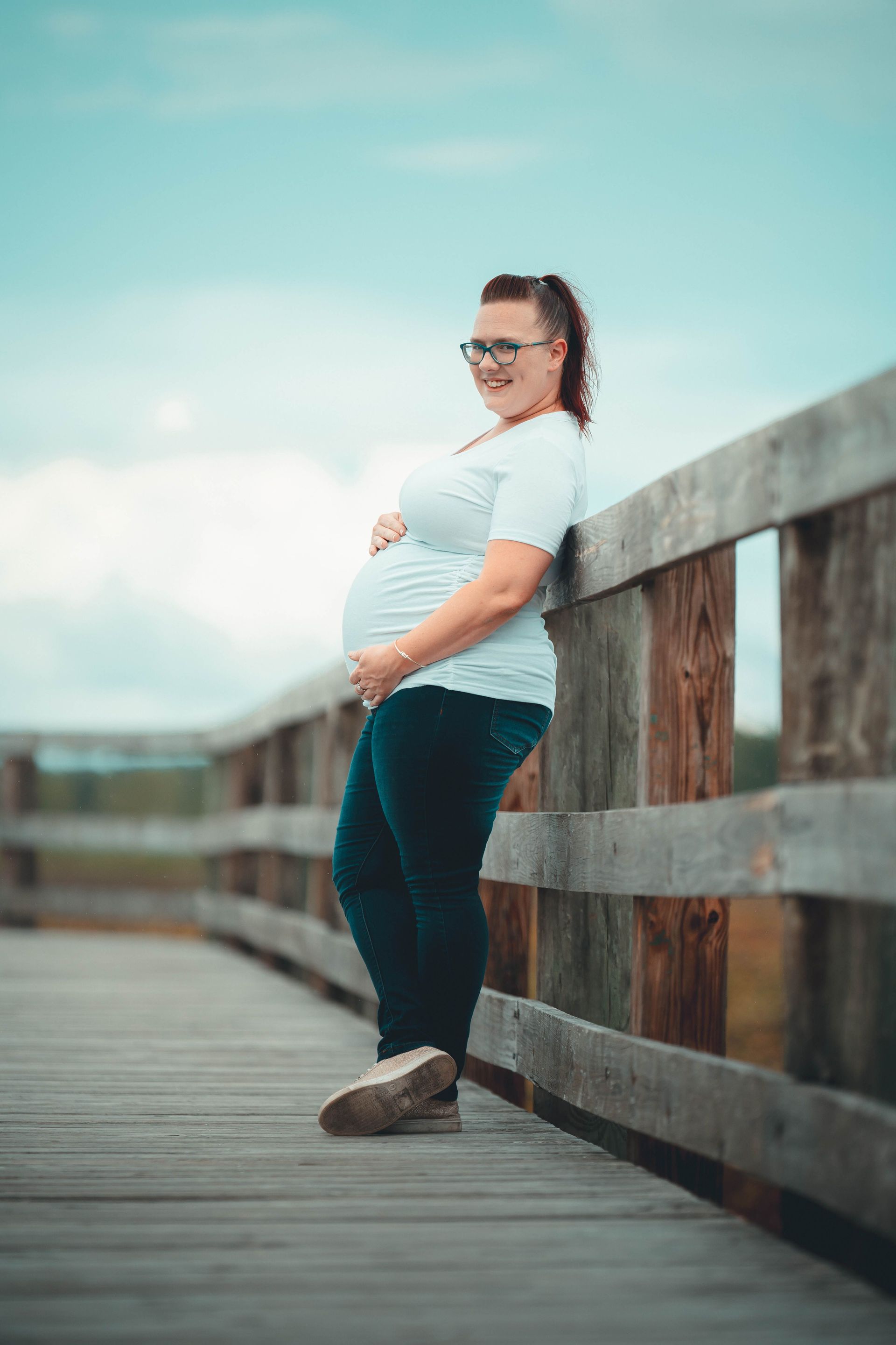 Pregnant person leaning on a wooden boardwalk railing under a blue sky