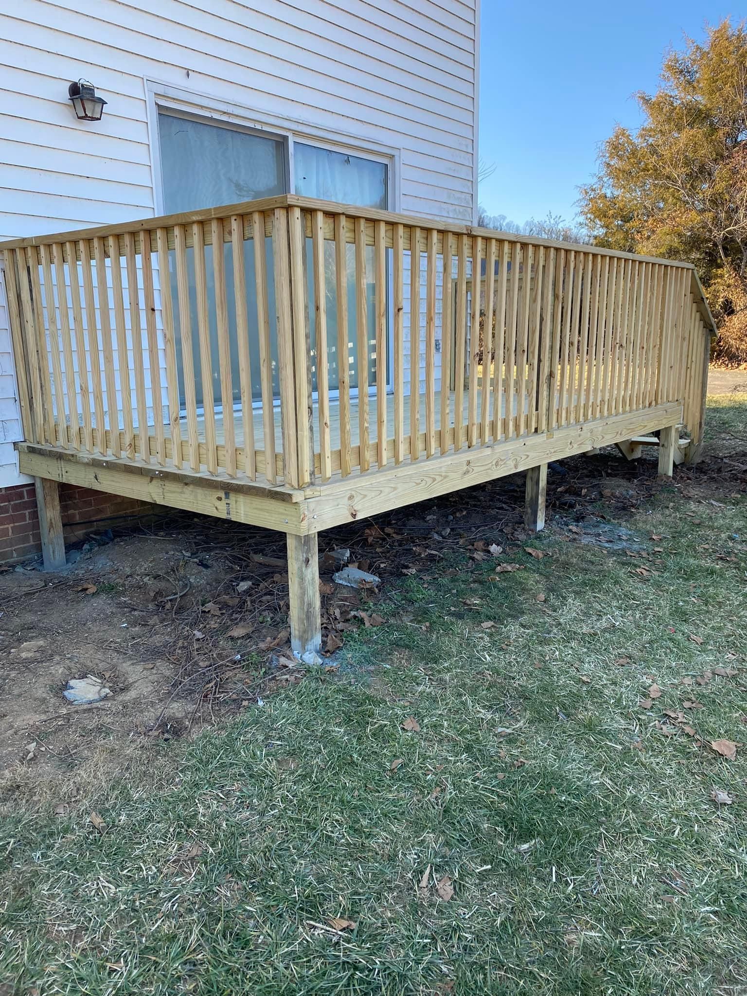 A newly constructed wooden deck with railings attached to the side of a light-colored house exterior.