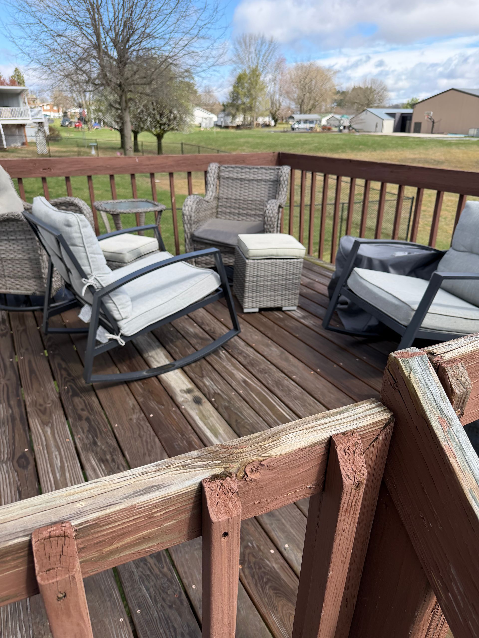Patio deck with cushioned chairs, wicker ottoman, and view of a grassy yard and houses beyond