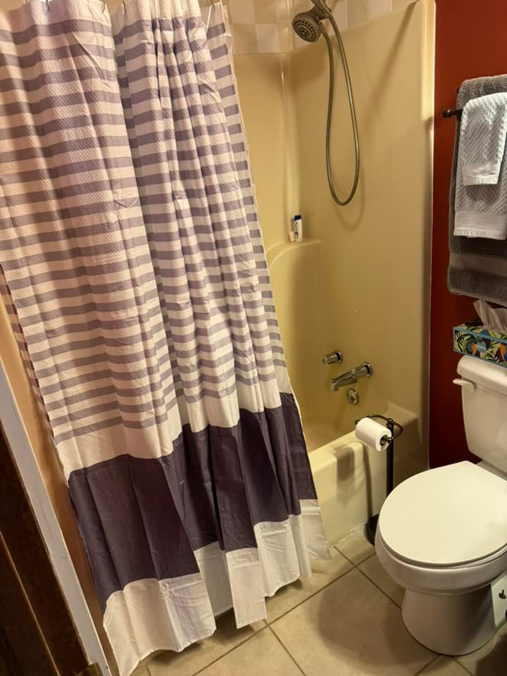 A bathroom featuring a shower with a striped blue and white curtain, beige tub fixtures, and a white toilet.