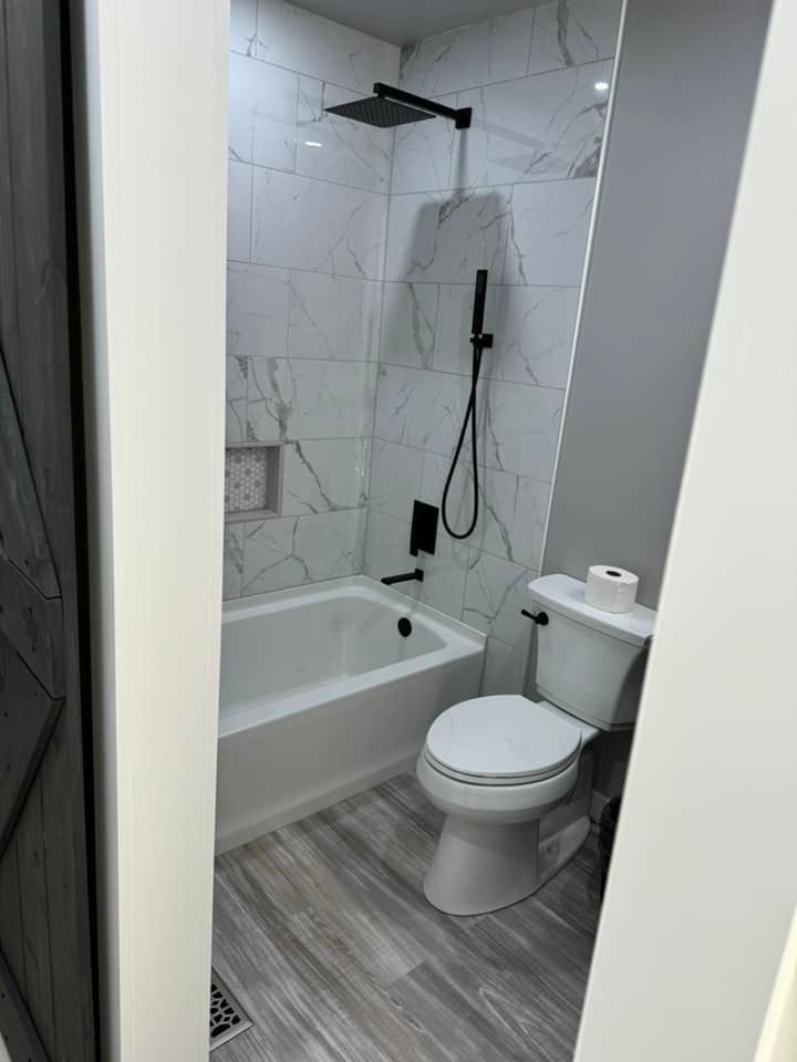 Modern bathroom featuring a white bathtub with marble-tiled walls, a black rainfall showerhead, and a white toilet.