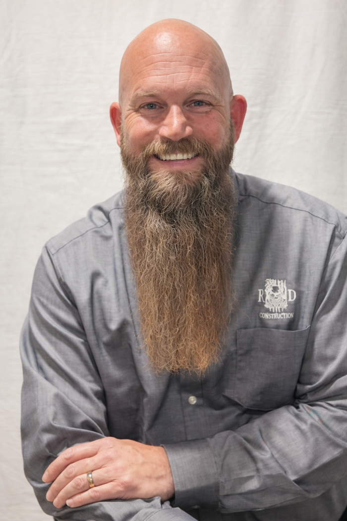 Email Robert Robert Booher is smiling man with a long beard wearing a gray button-down shirt stands against a plain white background.