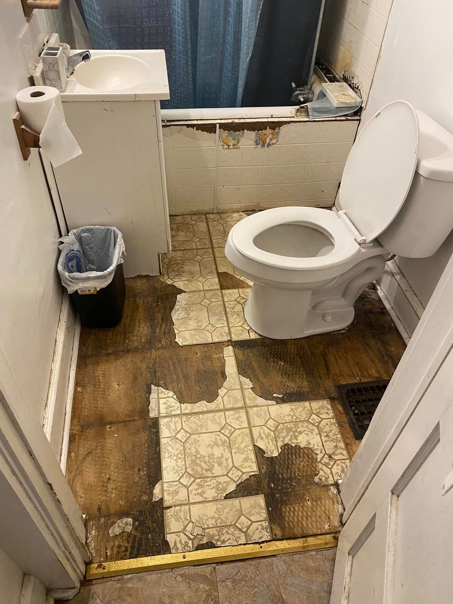 A small, worn bathroom with a white toilet, pedestal sink, and damaged flooring in need of repair.