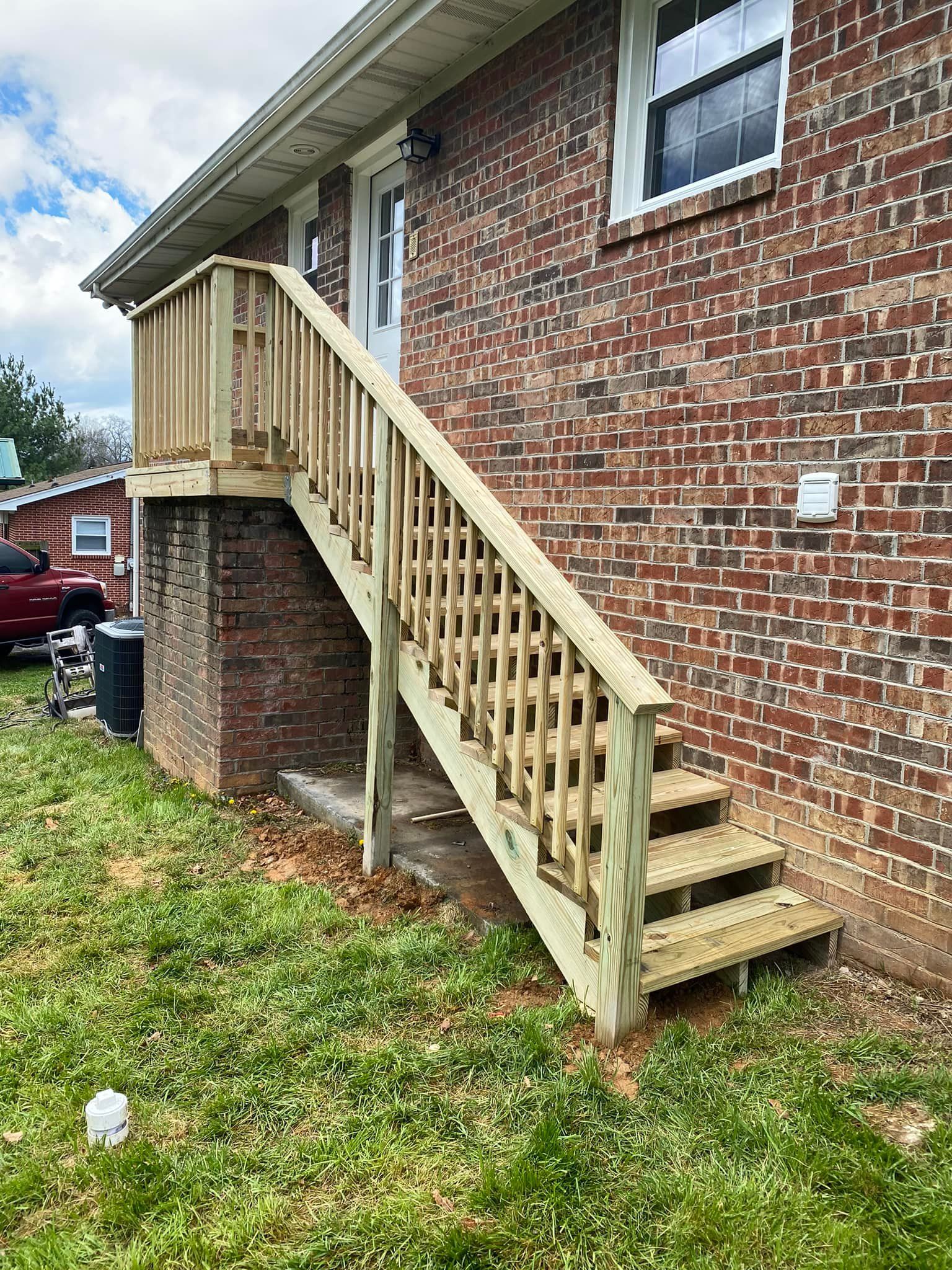 A new wooden staircase with railings attached to the side of a red brick house above a brick base.