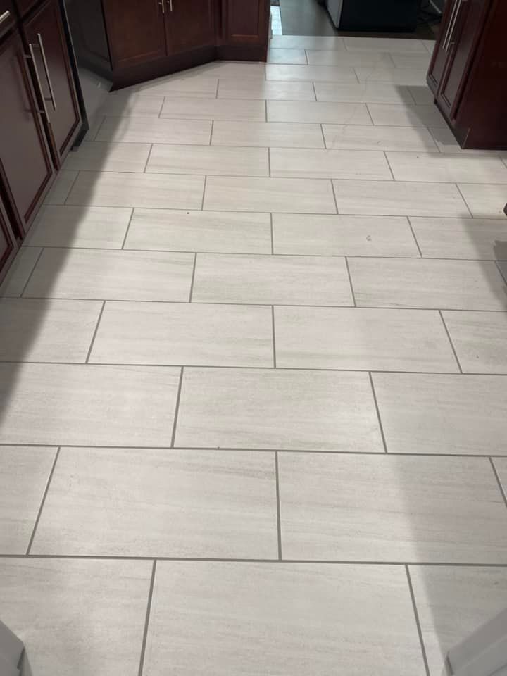 A kitchen floor featuring light-colored, rectangular tiles arranged in a staggered pattern between dark wood cabinets.