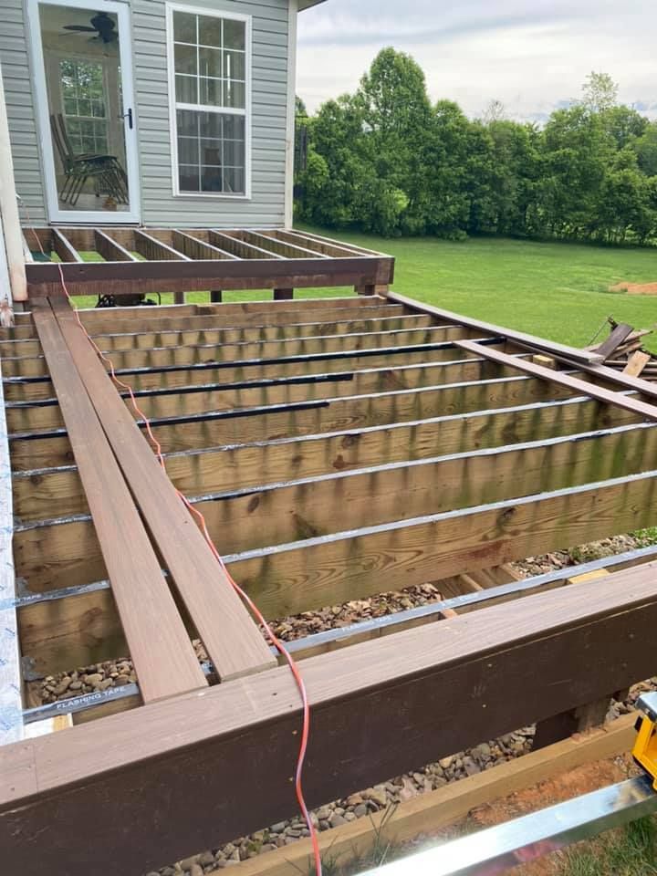An unfinished wooden deck under construction, showing exposed joists and some installed brown composite trim boards.