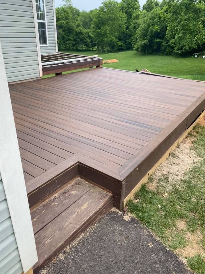 A brown composite deck attached to a house with a single step leading down to a paved walkway and a grassy lawn.