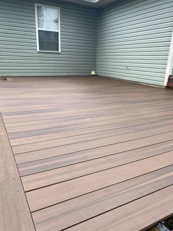 A wide-angle view of a brown composite deck with horizontal planks against a house with light green horizontal siding.