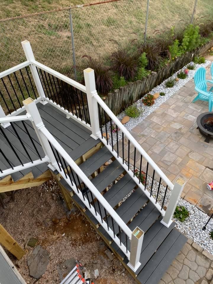 Gray composite deck stairs with white railings and black balusters leading to a stone patio with outdoor seating.