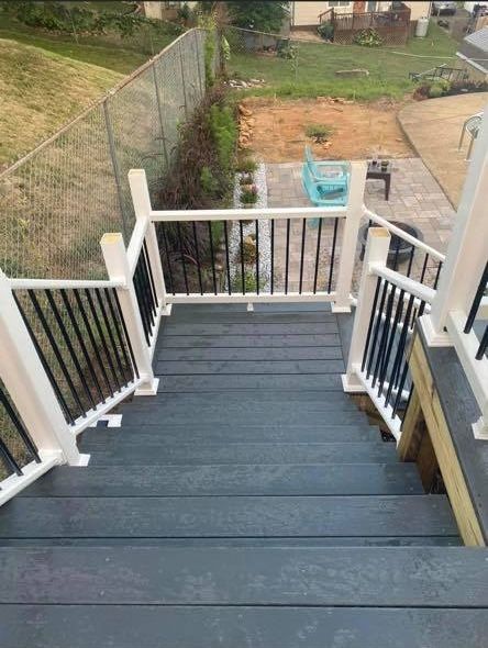 A straight outdoor staircase with dark gray treads and white railings with black balusters, overlooking a patio area.