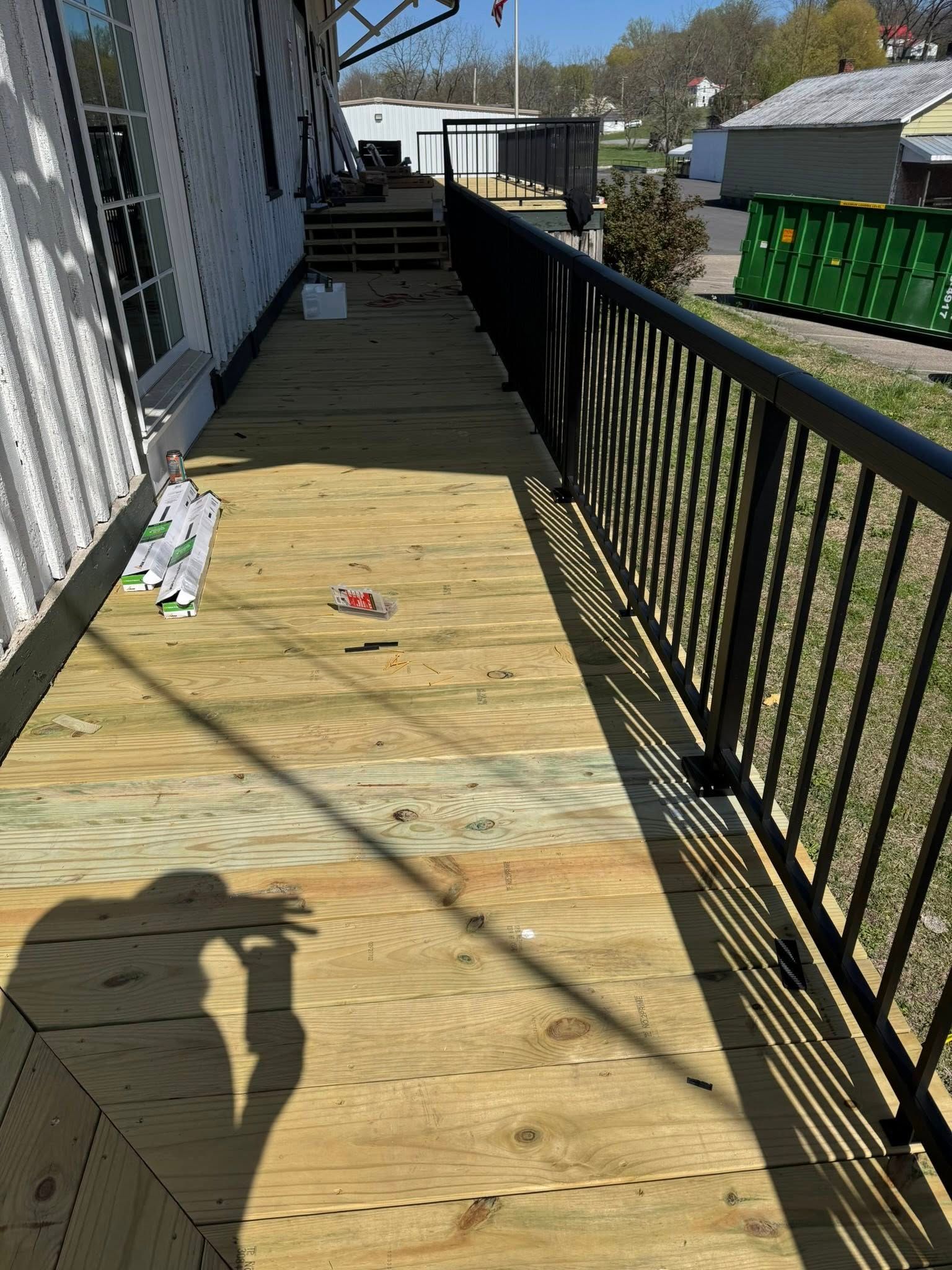 An after image of the freshly installed wooden deck with a black railing along the side of a building,