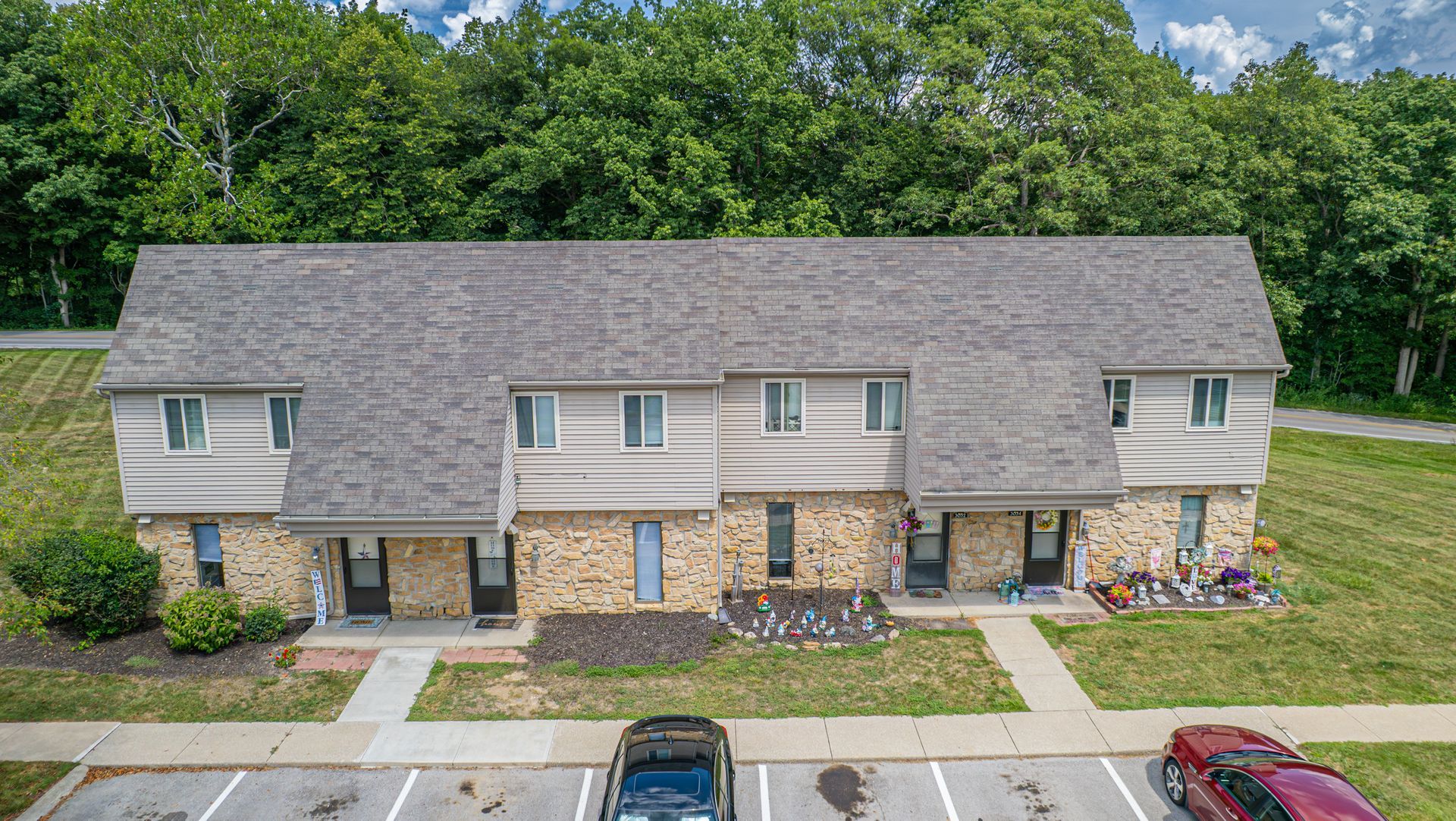 Multi-unit residential building with stone and wood siding, gray roof, and parking area.