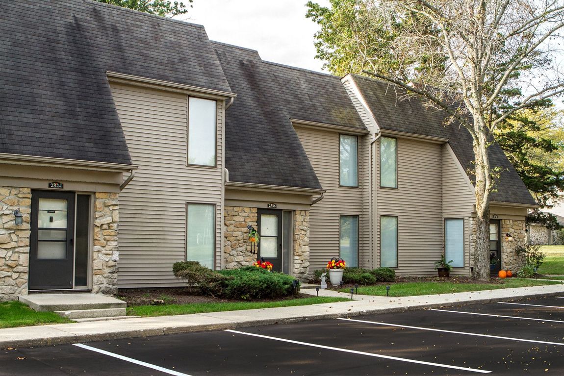 Townhouses with gray roofs, tan siding, and stone accents next to a parking lot.
