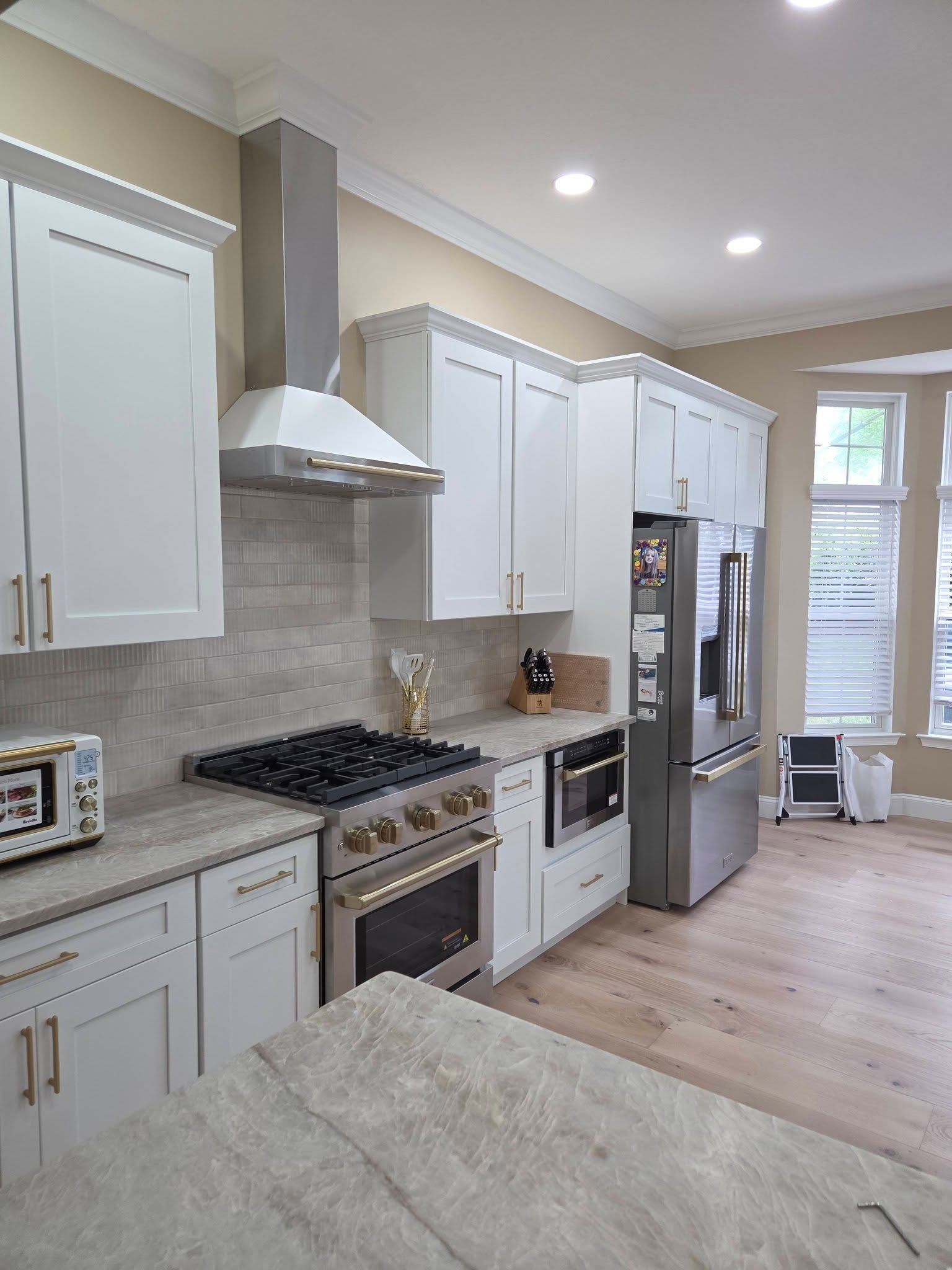 Bright kitchen with white cabinets, stainless steel appliances, marble island, and light wood floor
