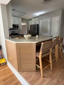 Kitchen with curved island, two wooden chairs, stainless fridge, and white cabinets on hardwood floor.