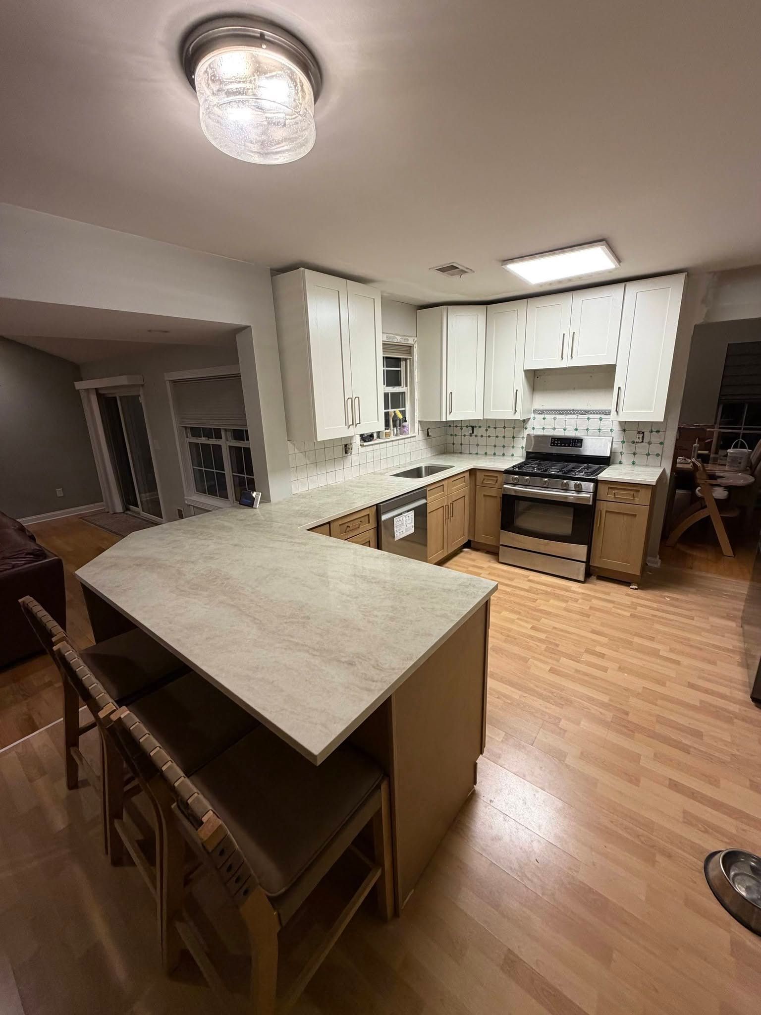 Kitchen with white cabinets, island counter, wood floors, and a white stove under bright ceiling lights.
