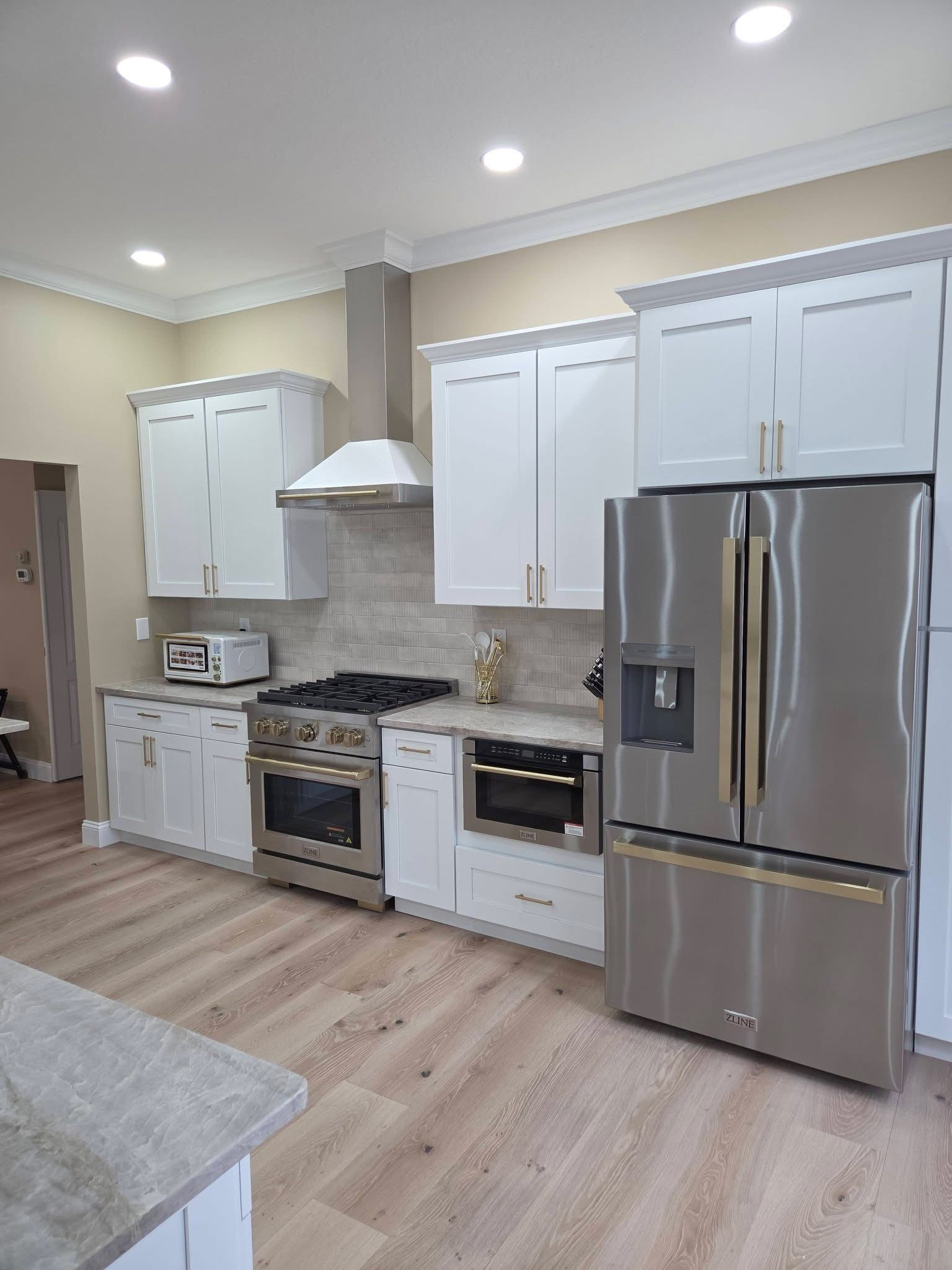Modern kitchen with white cabinets, stainless steel appliances, and light wood flooring