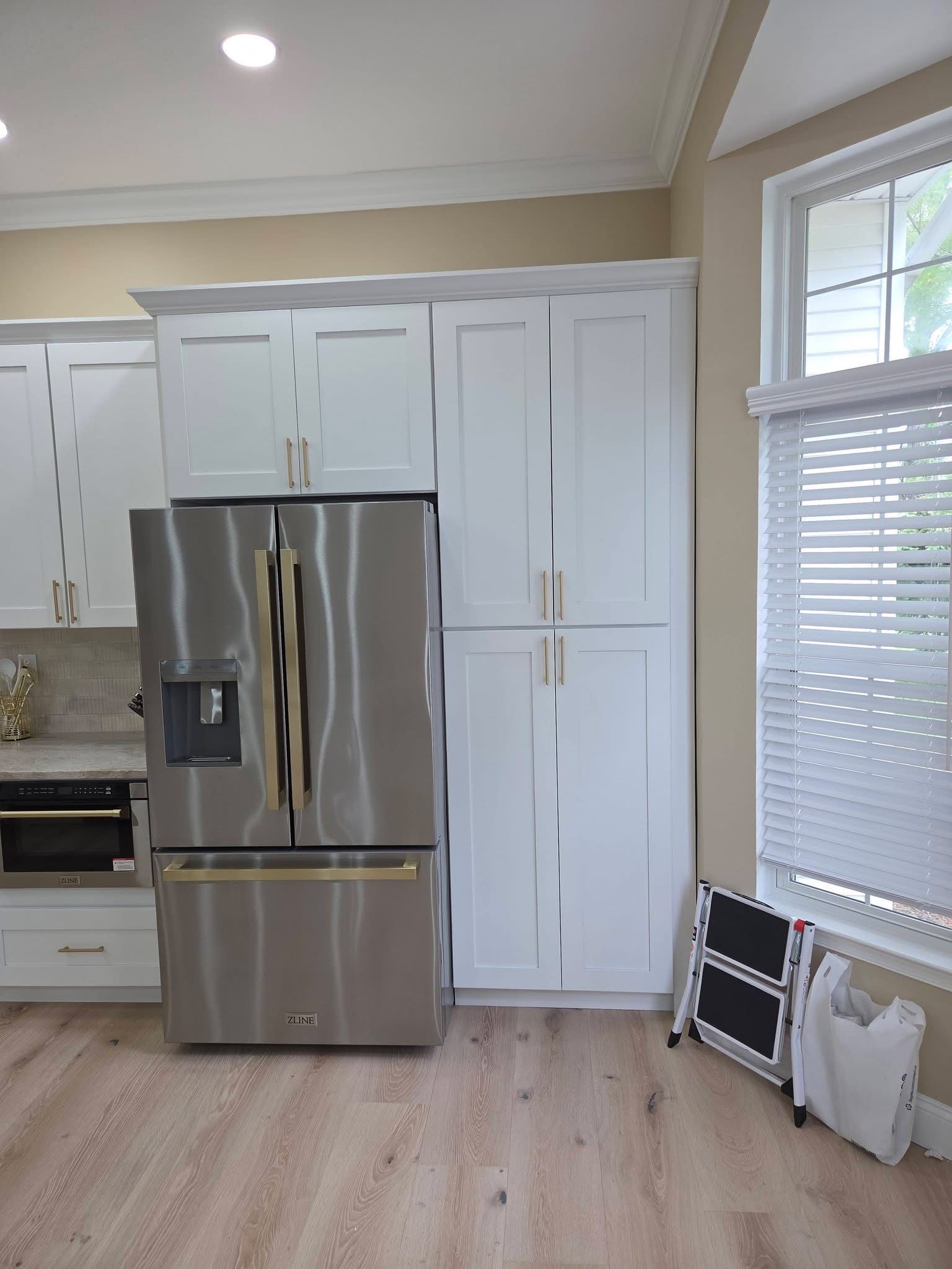 Bright kitchen with white cabinets, stainless steel fridge, and a window with blinds.