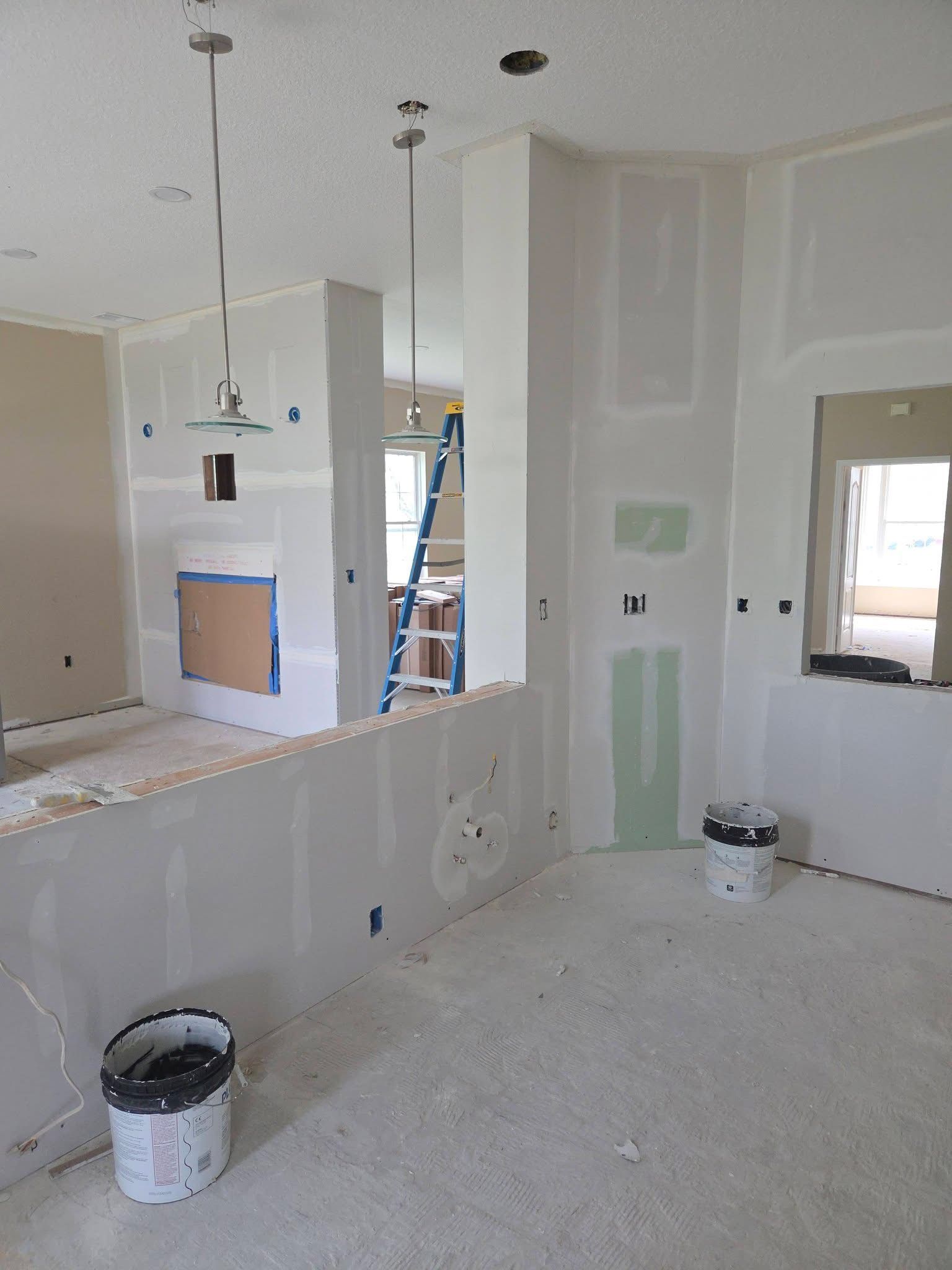 Unfinished kitchen with drywall, paint buckets, and a window during renovation.