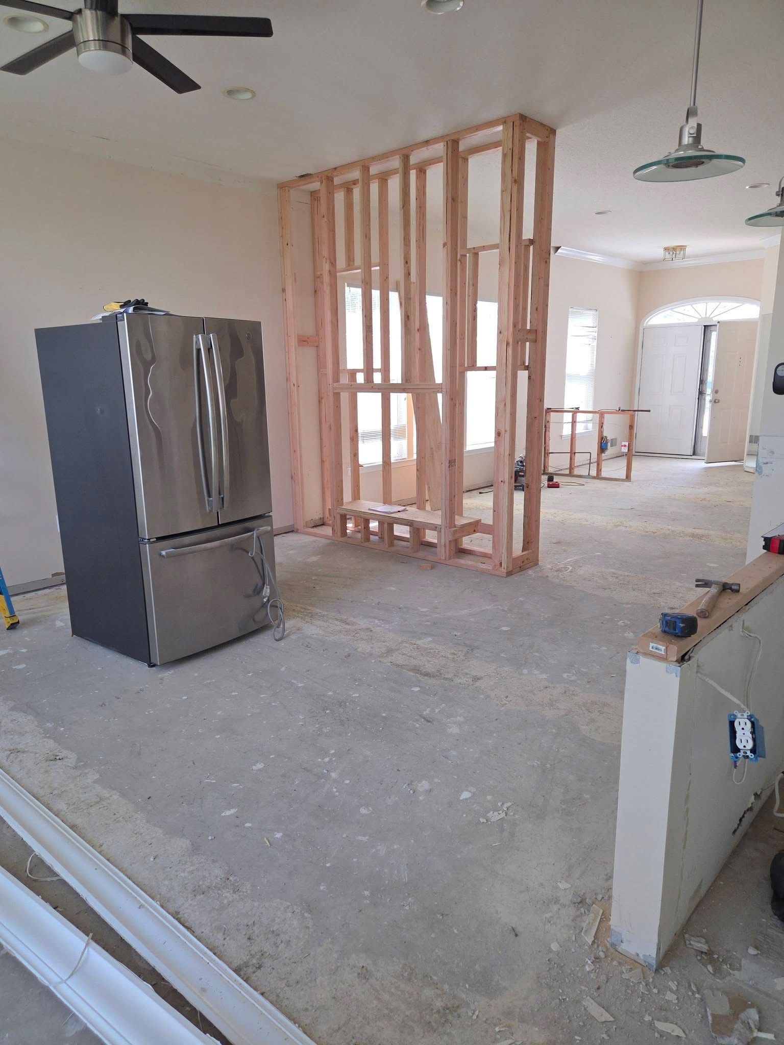 Unfinished home interior with exposed framing, refrigerator, and ceiling fans in an empty room
