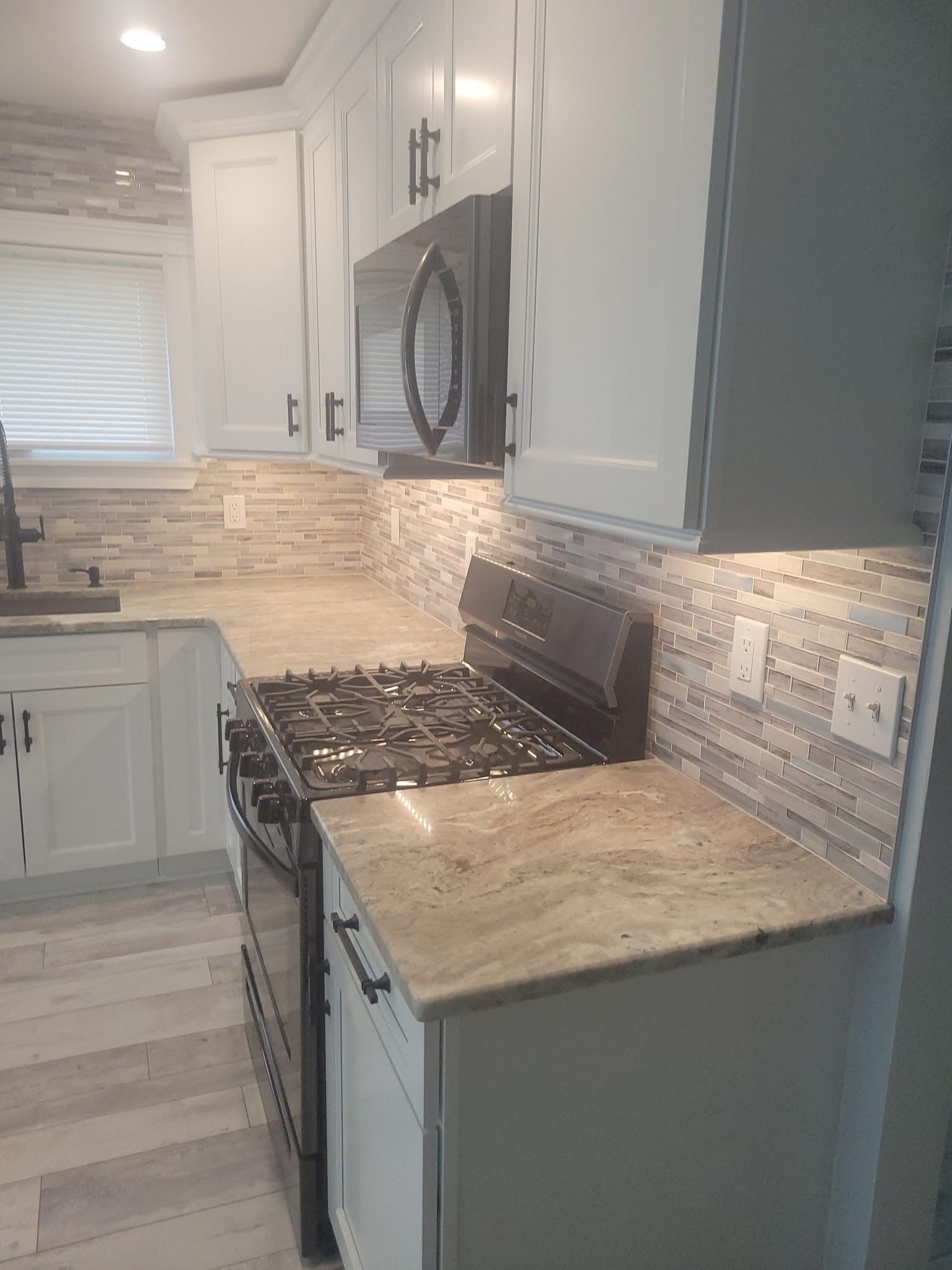 Modern kitchen with gray cabinets, beige countertops, white tile backsplash, and stainless gas stove.