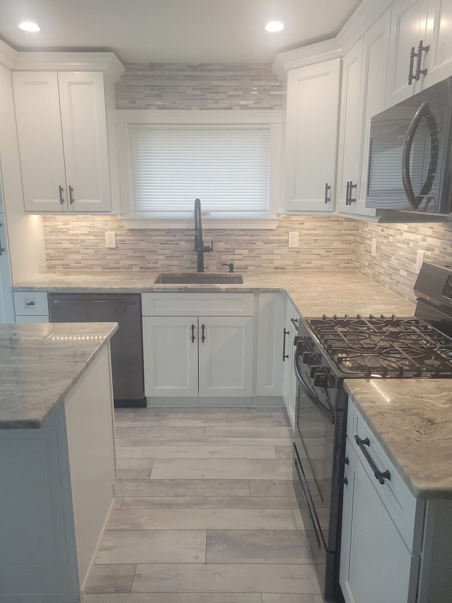 Modern white kitchen with gray tile backsplash, farmhouse sink, gas stove, and central island.