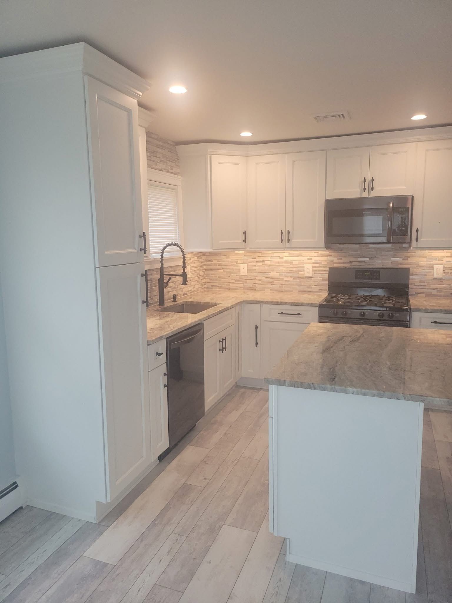Bright modern kitchen with white cabinets, stone countertops, island, stainless appliances, and light wood floors