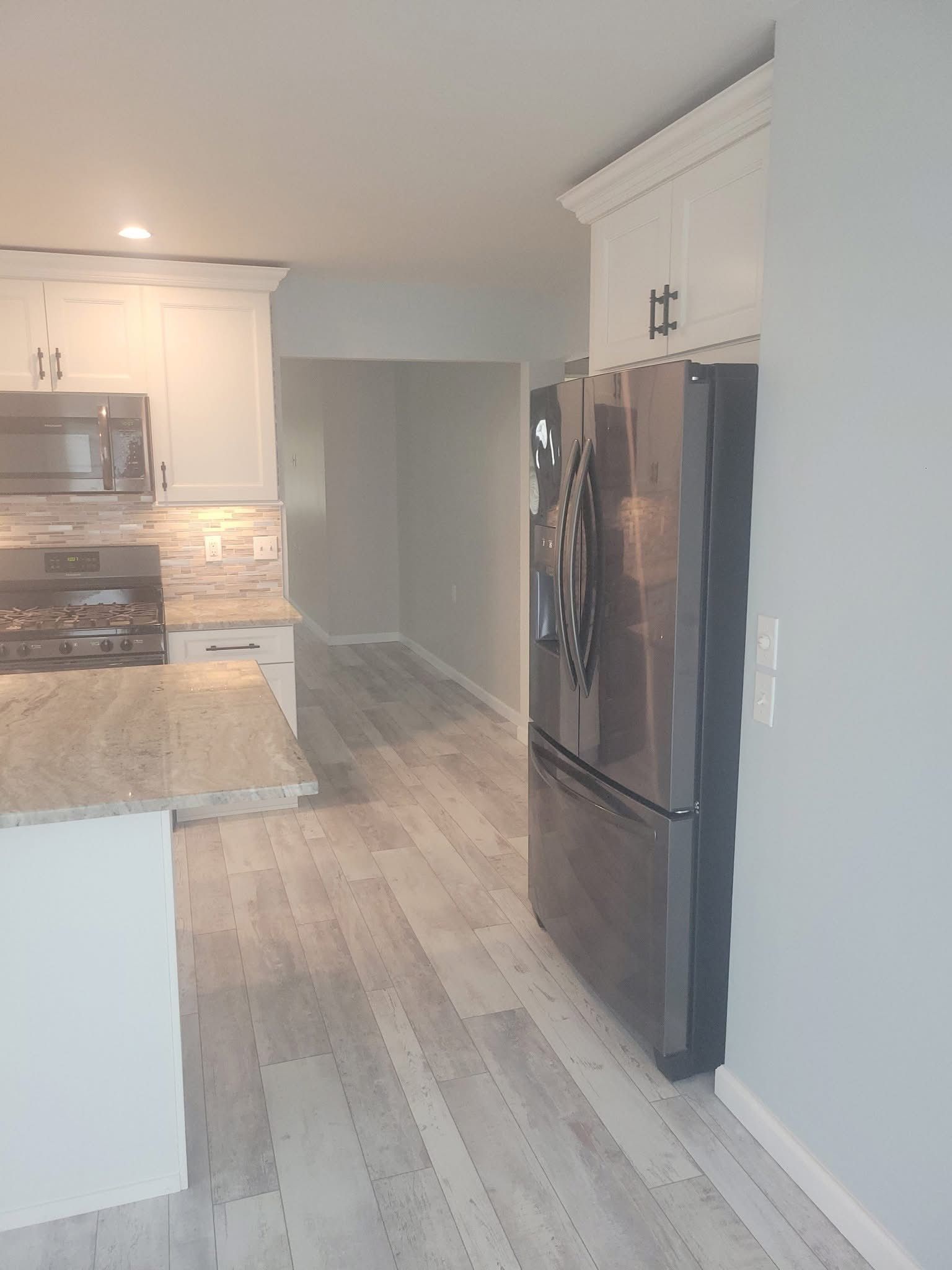 Modern kitchen with white cabinets, light wood floors, granite counters, and stainless steel appliances