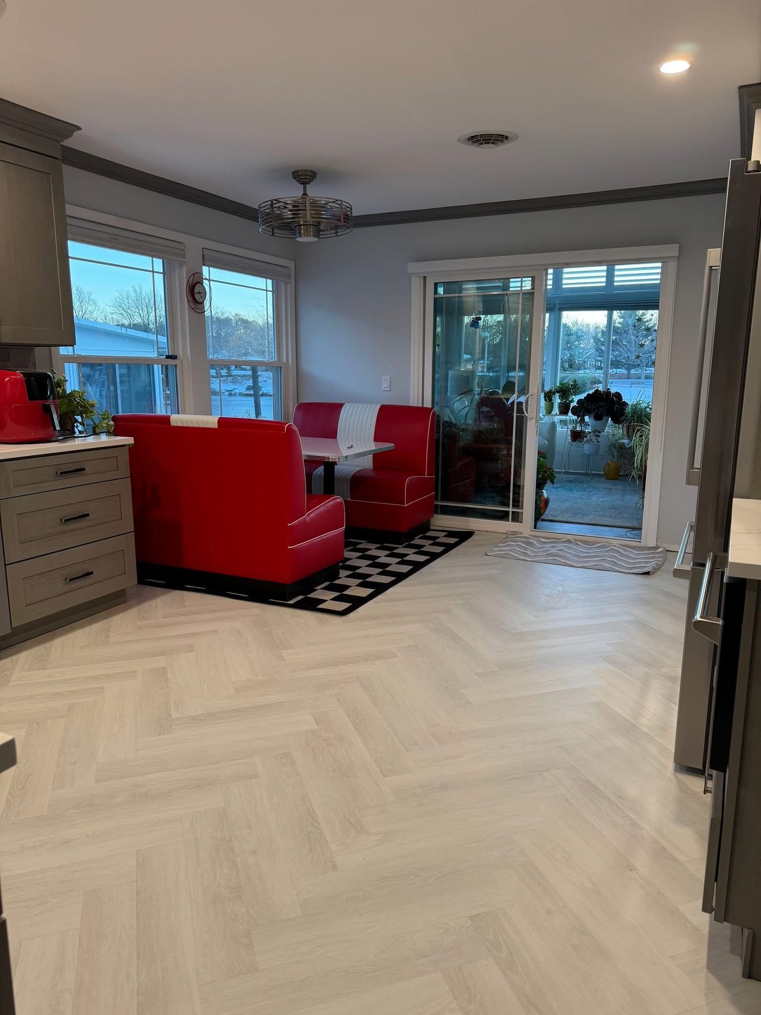 Modern kitchen and dining area with red chairs, herringbone wood floor, and sliding glass doors to a patio