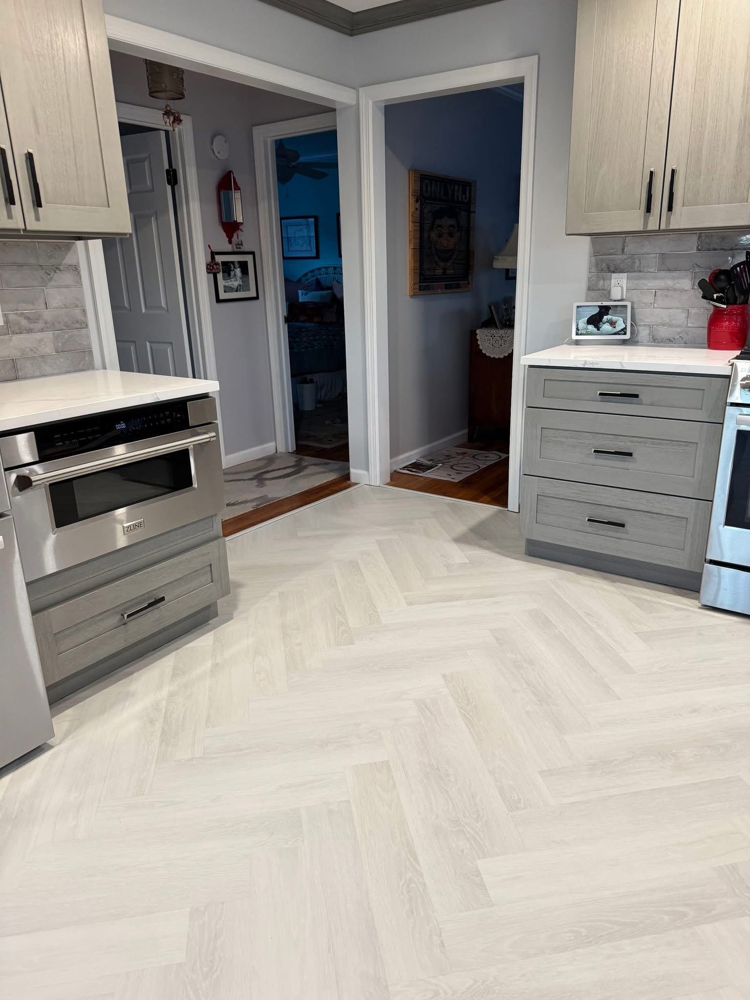 Modern kitchen with light wood cabinets, white patterned floor, and open doorway to a dim hall