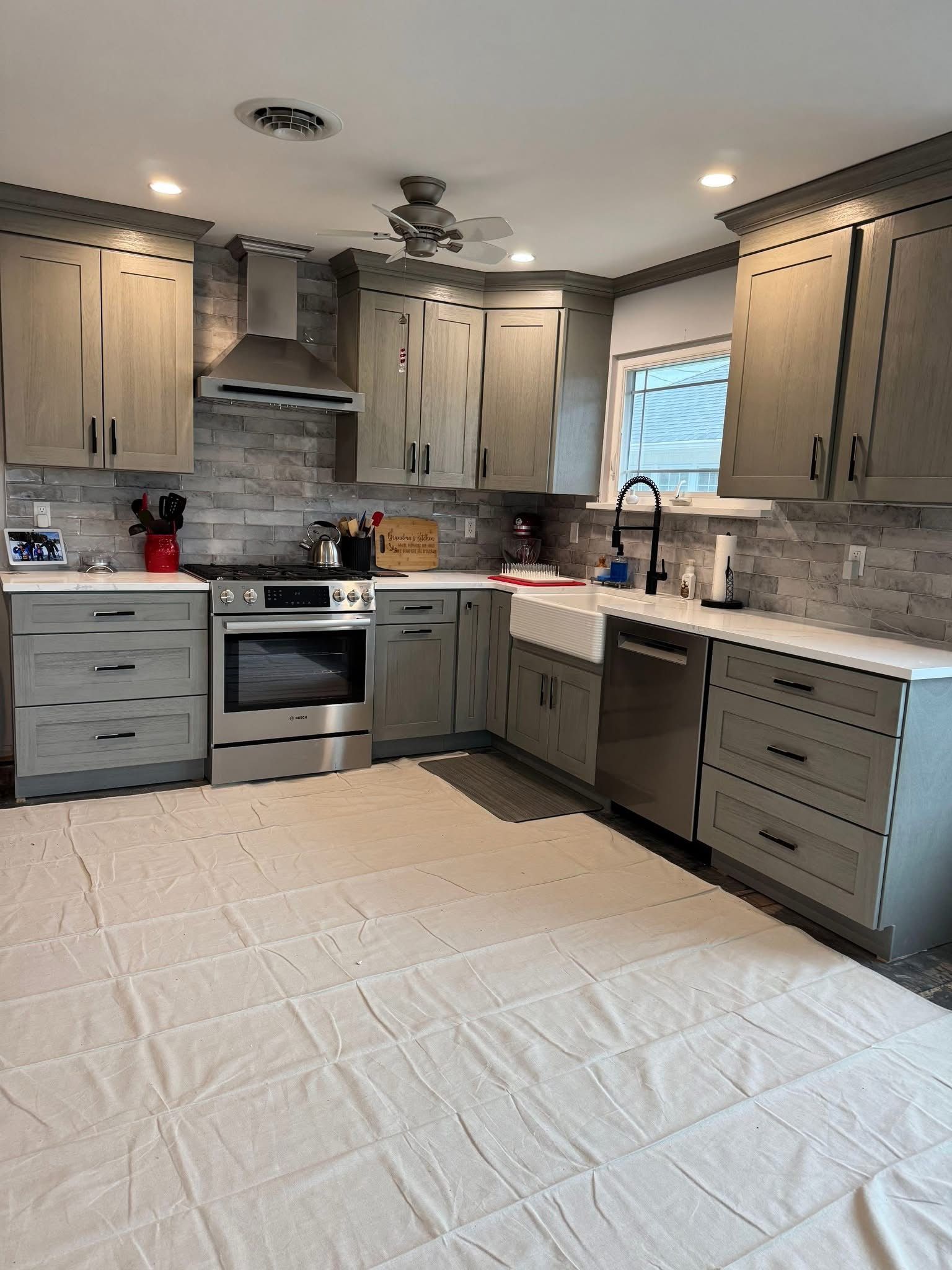 Newly renovated kitchen with gray cabinets, stainless steel appliances, and white protective floor covering