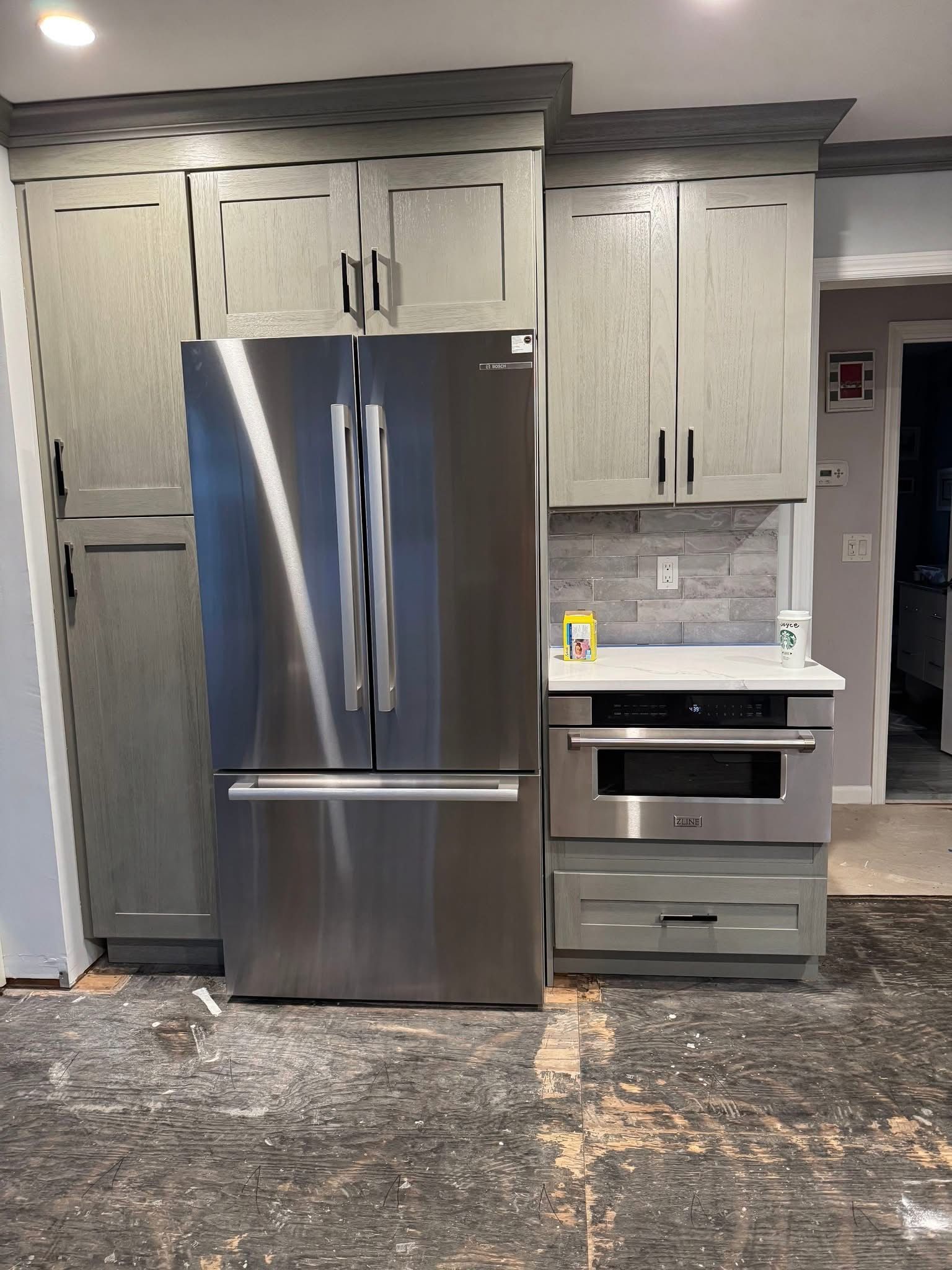 Modern kitchen with stainless steel refrigerator, gray cabinets, and a built-in oven.