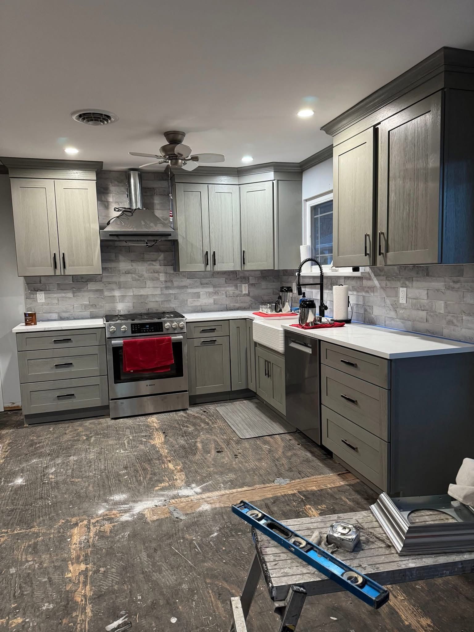 Modern kitchen under renovation with gray cabinets, red stove, backsplash tile, and scattered tools on the floor