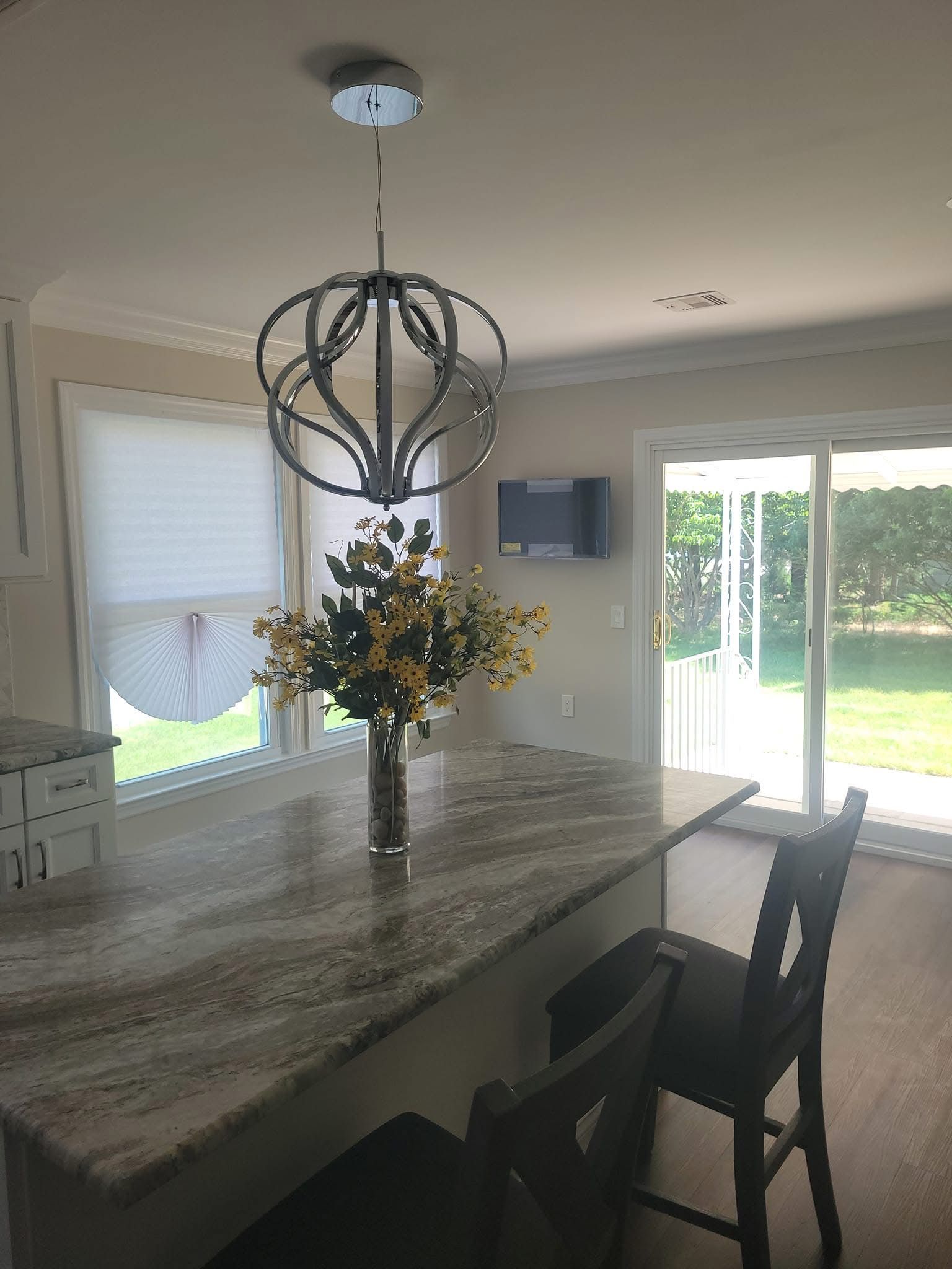 Kitchen with granite island, flower centerpiece, dark barstools, pendant light, and backyard view through glass doors