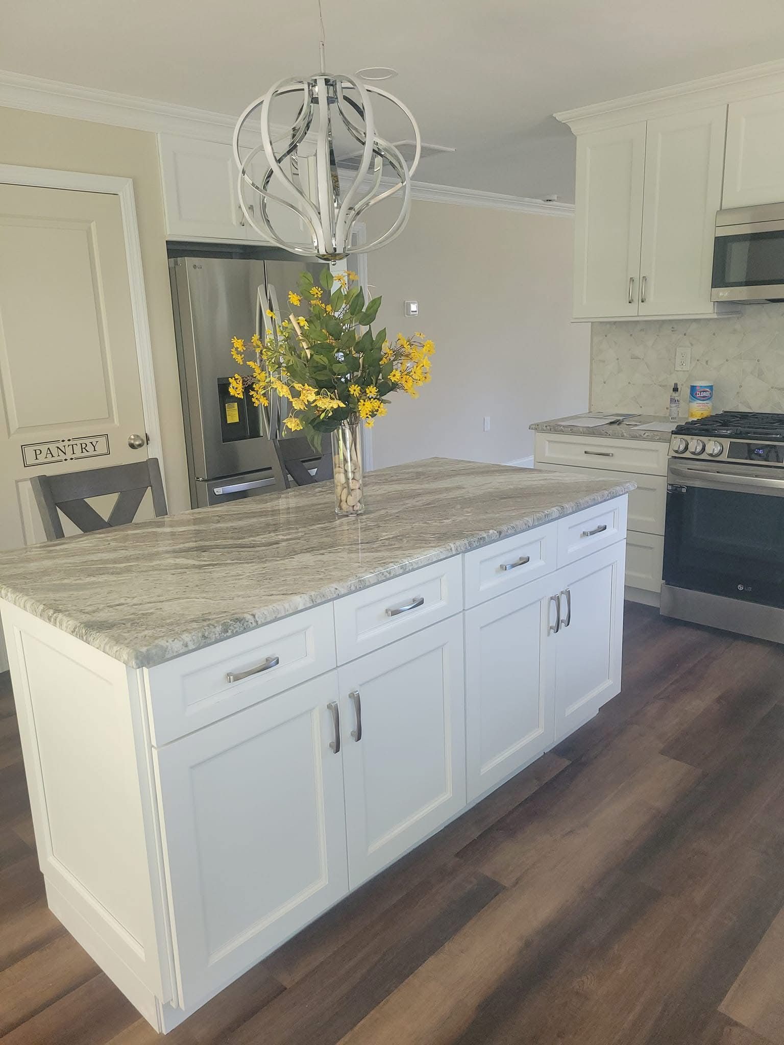 Bright kitchen with white cabinets, granite island, pendant light, and yellow flowers in a vase.