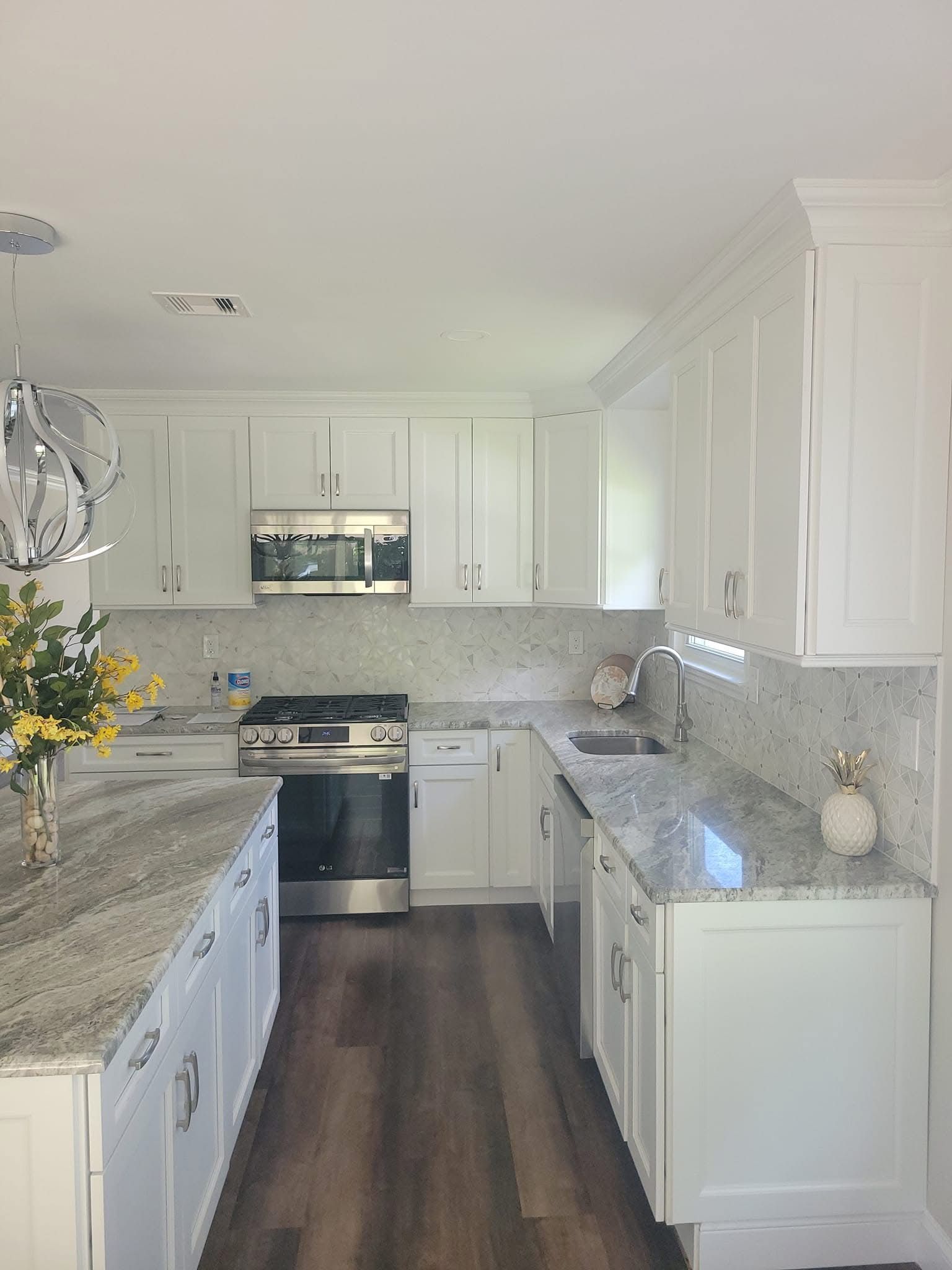 Bright white kitchen with granite countertops, stainless stove, and dark wood floors.