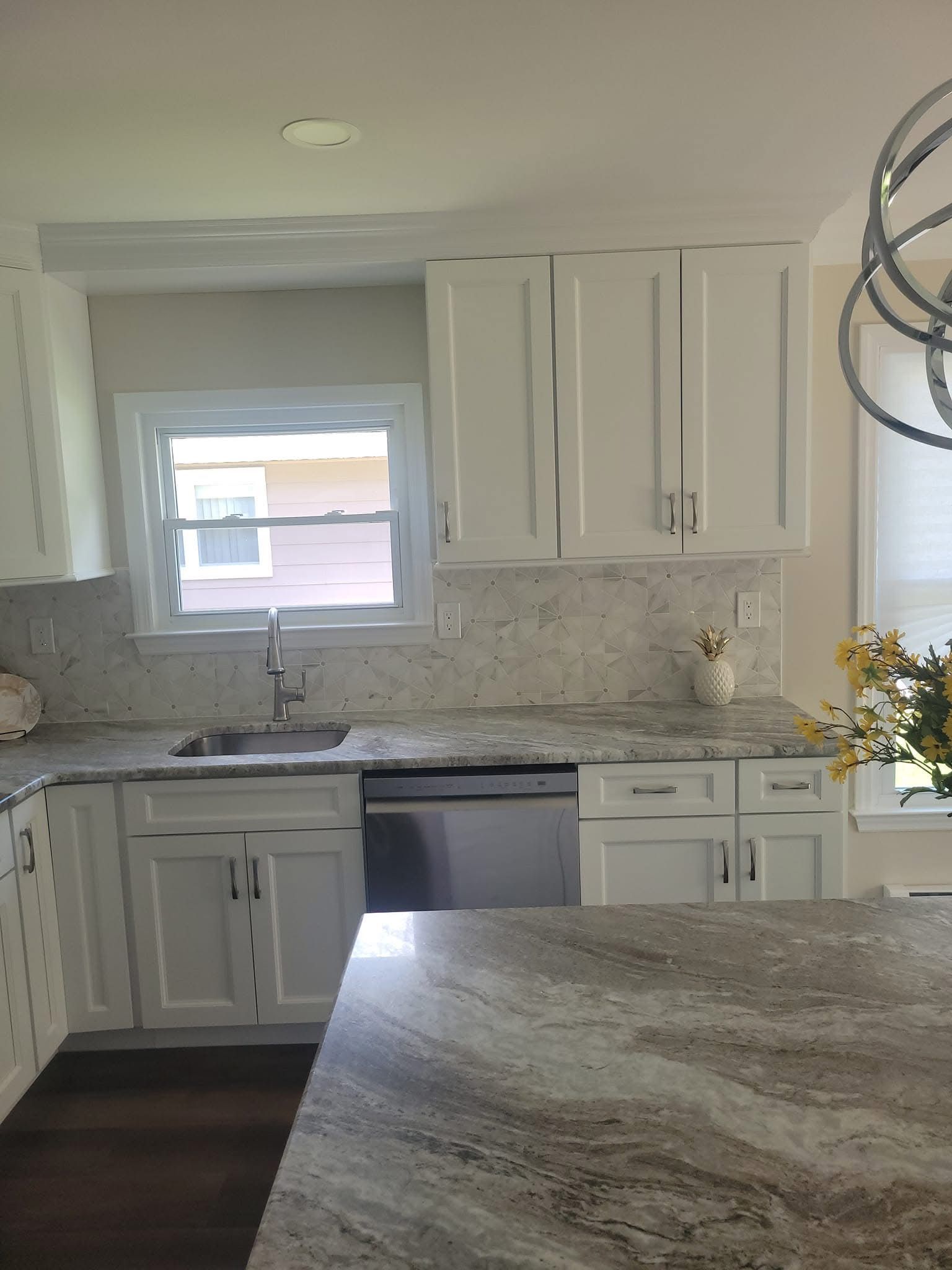Bright white kitchen with marble counters, window above sink, and dark wood floor.